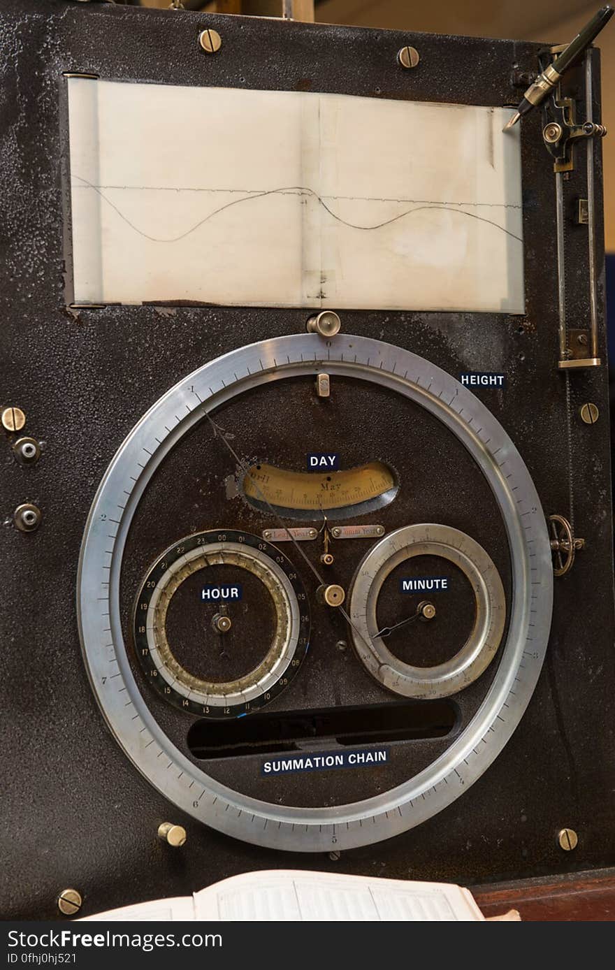 The output face of Tide Predicting Machine No. 2, a special purpose mechanical analog computer for predicting the height and time of high and low tides. The pen at the top draws the tide height as the paper moves beneath it. The dials below display the predicted tide height and the corresponding date and time. When the machine was in operation, the operator recorded the height and time of high and low tides, which were later reproduced in printed tide tables. The U.S. government used Tide Predicting Machine No. 2 from 1910 to 1965 to predict tides for ports around the world. The machine, also known as â€œOld Brass Brains,â€ uses an intricate arrangement of gears, pulleys, chains, slides, and other mechanical components to perform the computations. A person using the machine would require 2-3 days to compute a yearâ€™s tides at one location. A person performing the same calculations by hand would require hundreds of days to perform the work. The machine is 10.8 feet &#x28;3.3 m&#x29; long, 6.2 feet &#x28;1.9 m&#x29; high, and 2.0 feet &#x28;0.61 m&#x29; wide and weighs approximately 2,500 pounds &#x28;1134 kg&#x29;. The operator powers the machine with a hand crank.