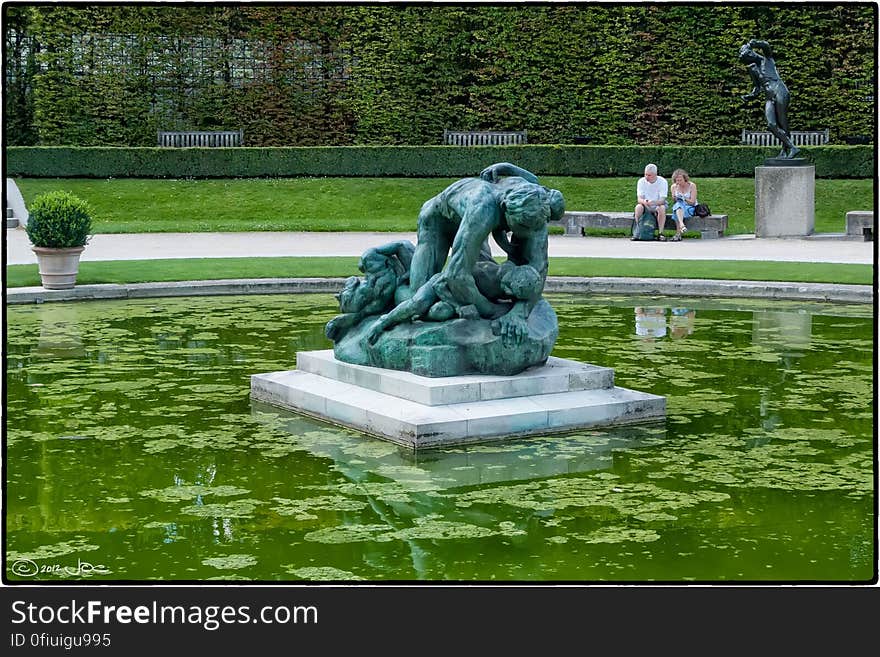 Tourists taking a break near the pond in the garden of the Rodin Museum in Paris. The central statue is &#x22;Ugolino and his children&#x22; and was created circa 1881. Driven crazy by hunger, Ugolino, Count of Gheradesca, devoured his dead children, a crime for which he was eternally damned.