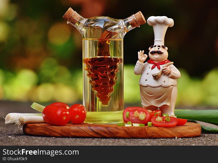 Chef Figurine Beside Clear Glass Bottle and Tomatoes