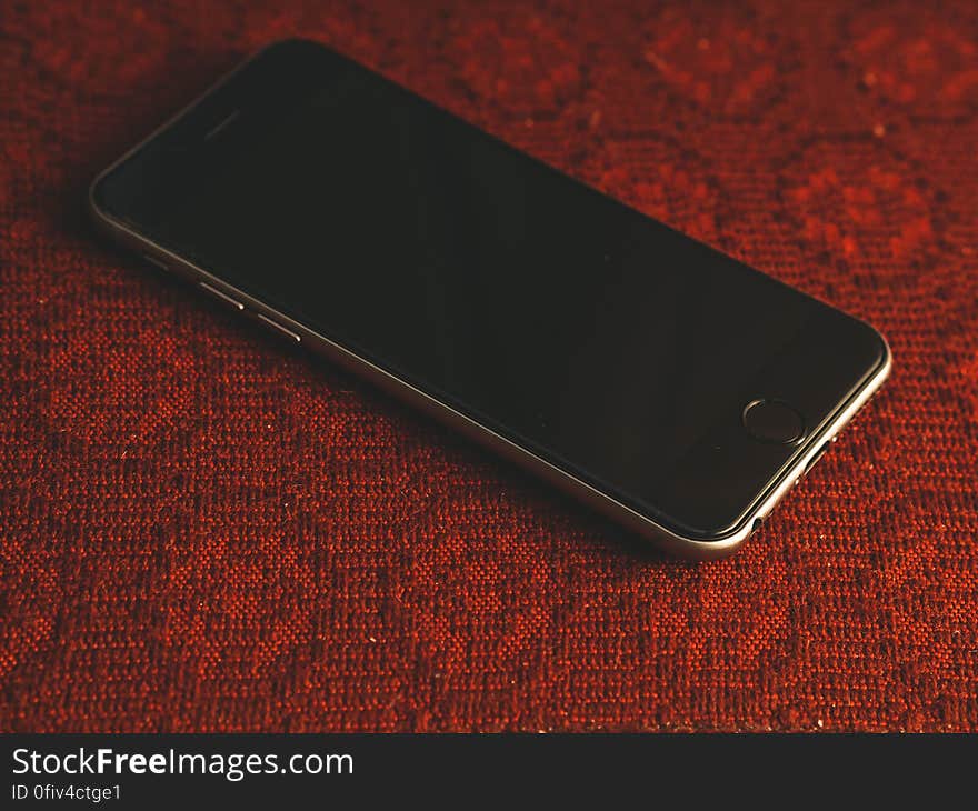 Mobile phone shown with black blank screen, chrome case, charger socket and volume control button, red woven background. Mobile phone shown with black blank screen, chrome case, charger socket and volume control button, red woven background.