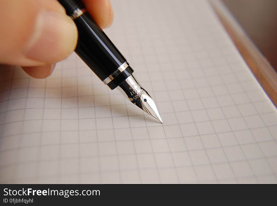 Hand of person about to write on graph paper with fountain pen. Hand of person about to write on graph paper with fountain pen.