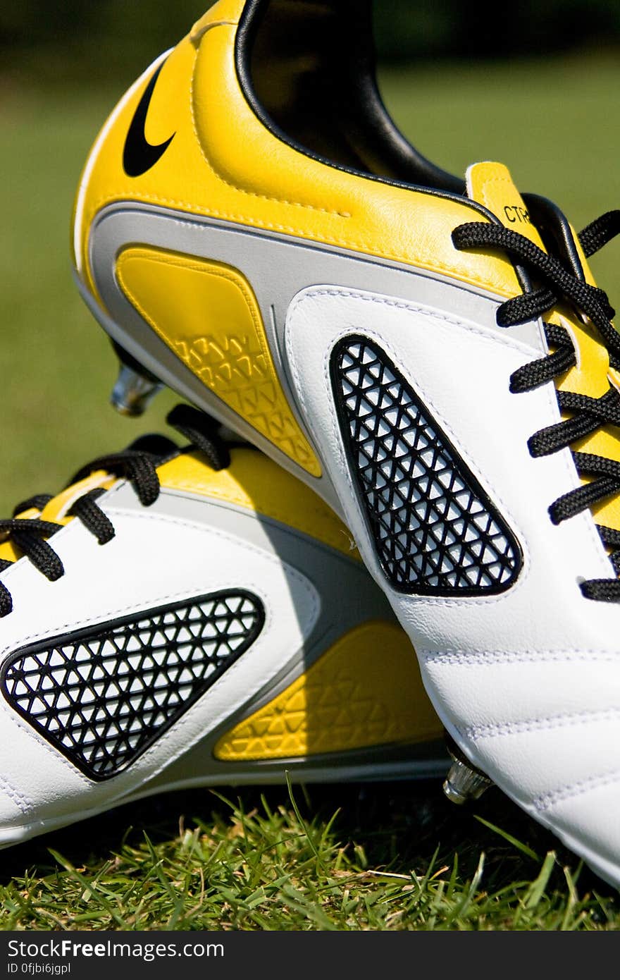 Side view of pair of yellow and white football boots on grass.