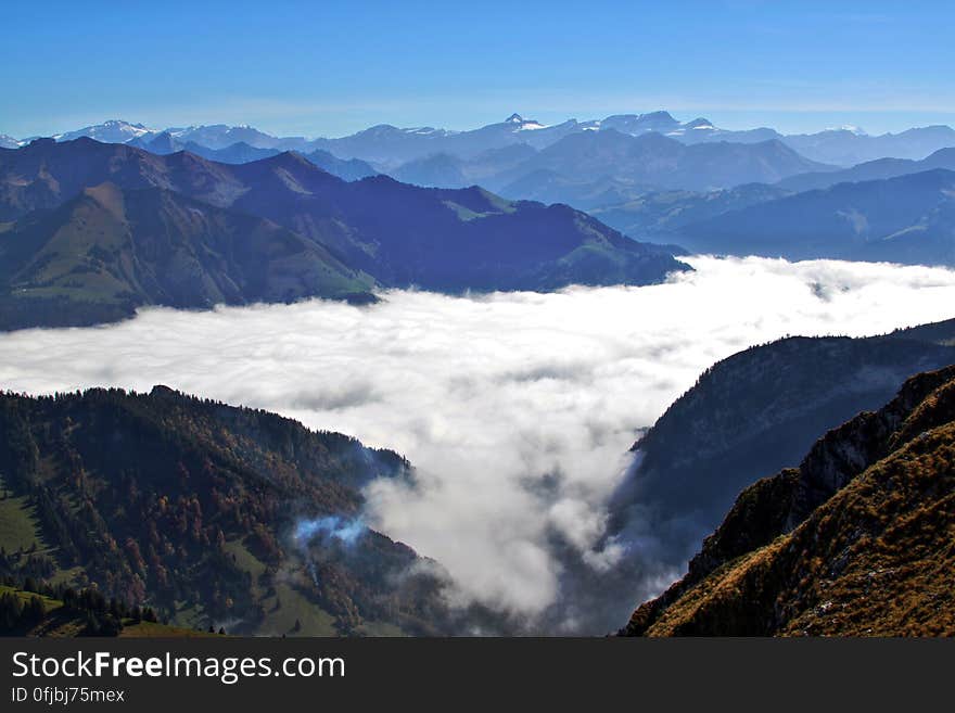 Aerial view over mountain peaks with fog in valley on sunny day with blue skies. Aerial view over mountain peaks with fog in valley on sunny day with blue skies.