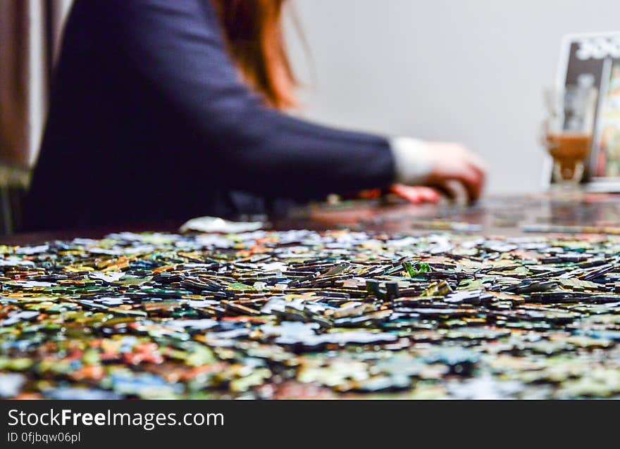 Woman with red hair and blue jacket doing a jigsaw puzzle on a table with selective focus on a few of the unplaced pieces. Woman with red hair and blue jacket doing a jigsaw puzzle on a table with selective focus on a few of the unplaced pieces.