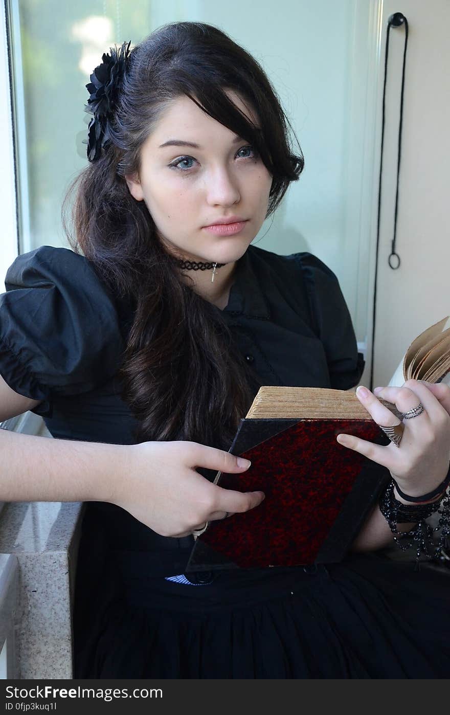 Woman With Black Hair and Wearing Black Cap Sleeve Dress Holding Book With Two Hands