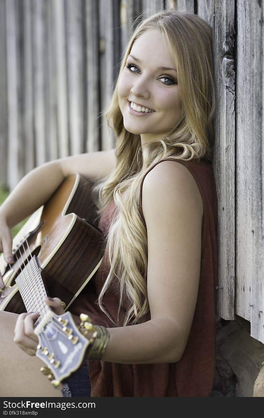 Woman in Maroon Tank Dress Playing Acoustic Guitar Near Wood