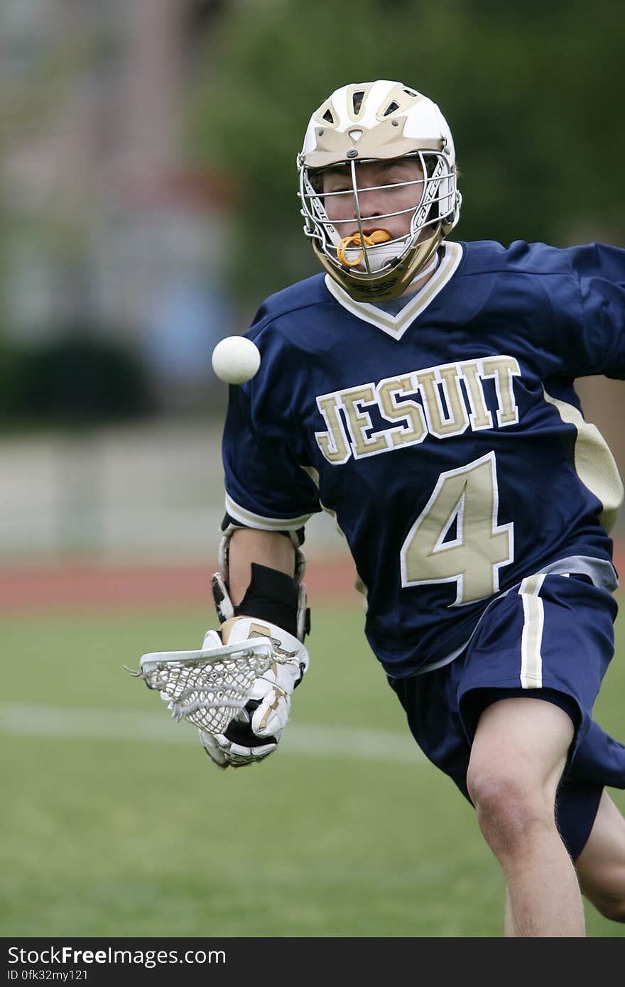 Man Holding Lacrosse Stick Running on Field during Daytime