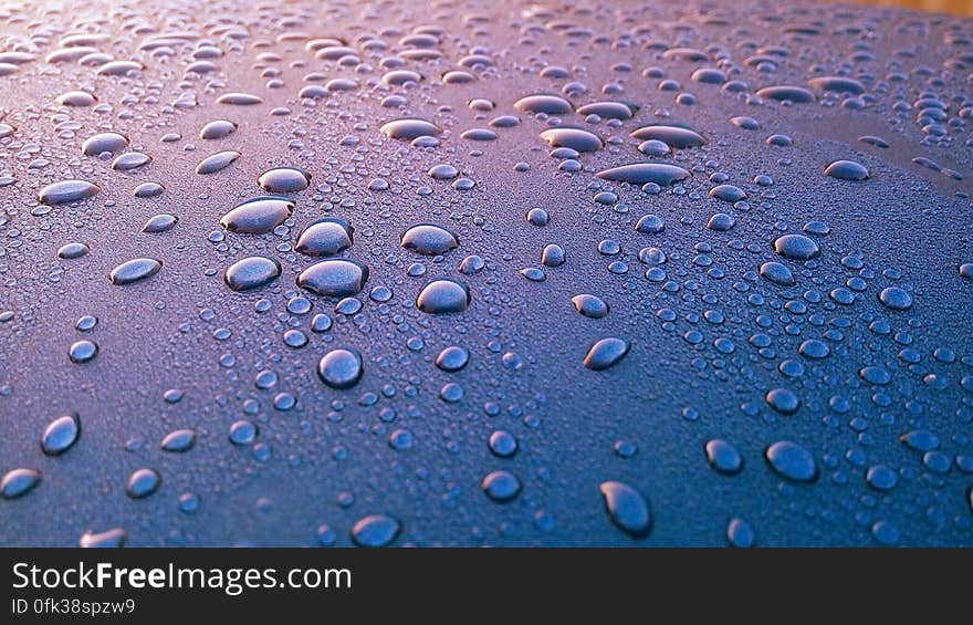 Close up of drops of water on shiny purple surface.