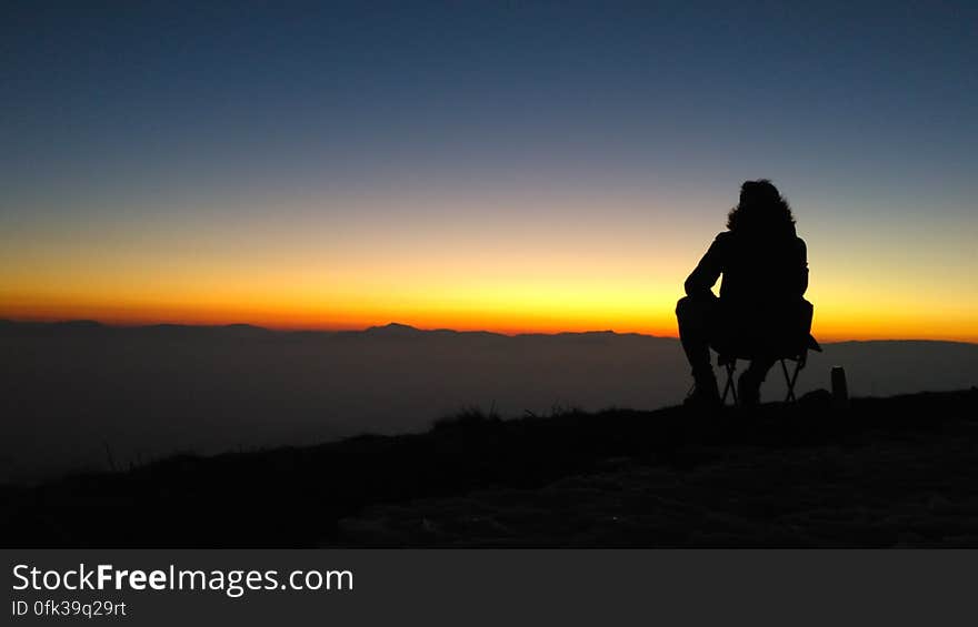 Silhouette of person sitting on edge of mountain overlooking valley at sunset. Silhouette of person sitting on edge of mountain overlooking valley at sunset.