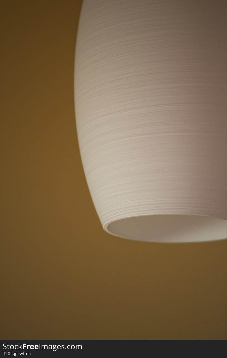 White ceramic ceiling lamp against mustard colored wall.