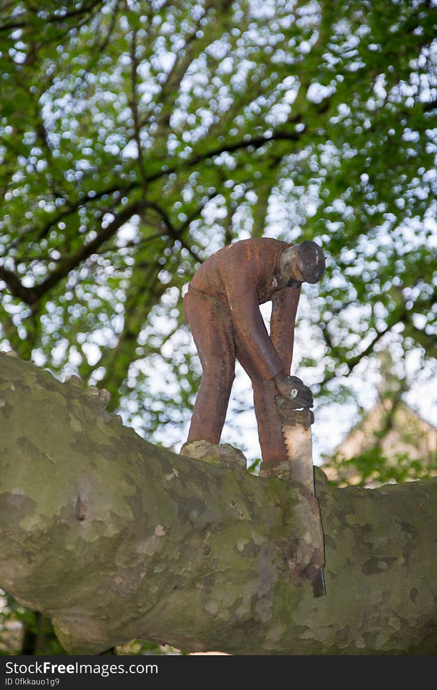 A mettalic work of art representing a woodcutter using a saw on a branch of a tree. A mettalic work of art representing a woodcutter using a saw on a branch of a tree.