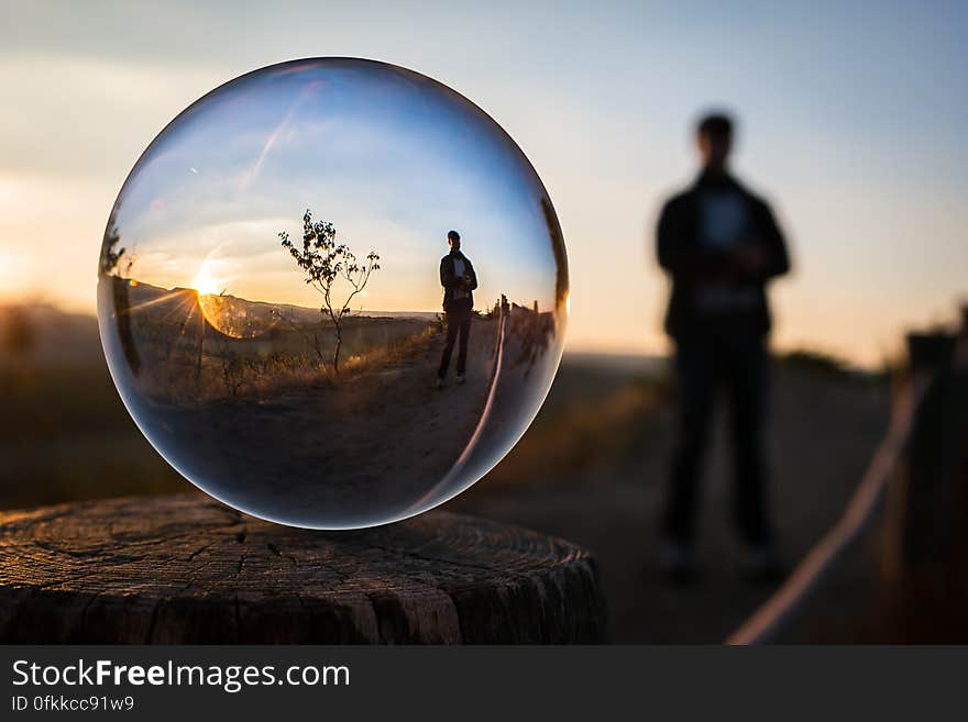 Silhouetted person in countryside at sunset viewed from back with front view of person reflected in glass ball. Silhouetted person in countryside at sunset viewed from back with front view of person reflected in glass ball.