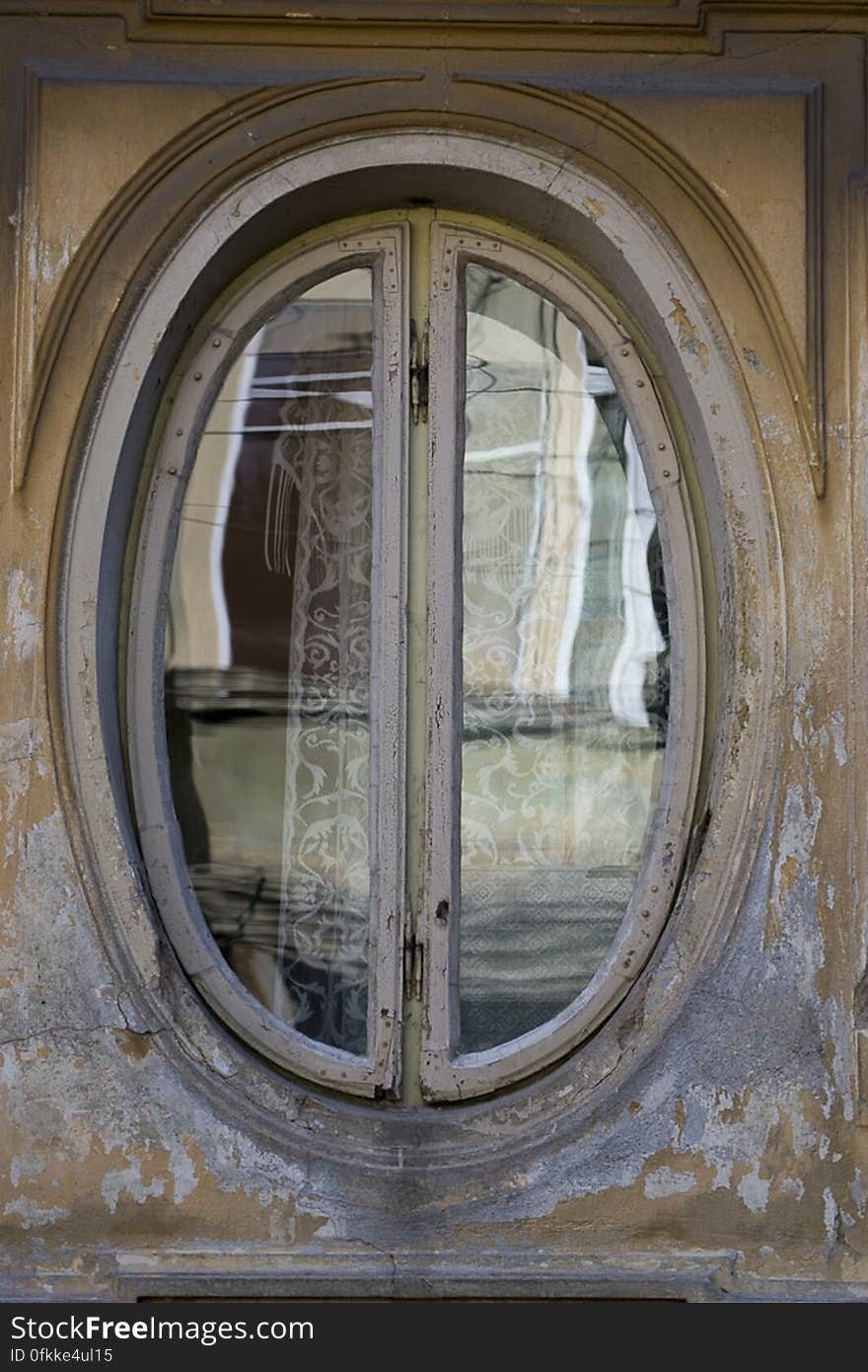 Photo of an oval shaped window frame on old house facade.