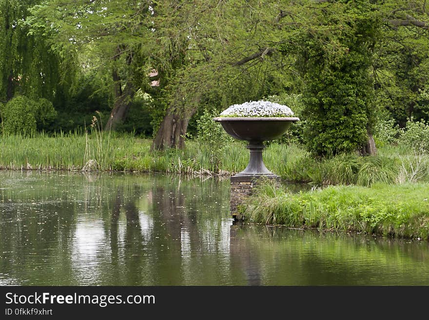 Cast iron flower pot on layered brick base by lake. Cast iron flower pot on layered brick base by lake.