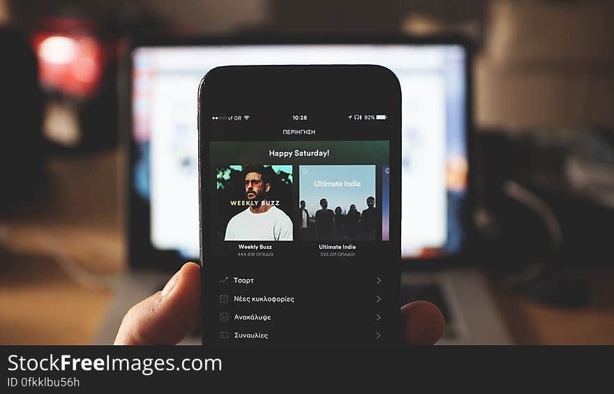 Hand of person holding smartphone with open music applications, large screen in background. Hand of person holding smartphone with open music applications, large screen in background.