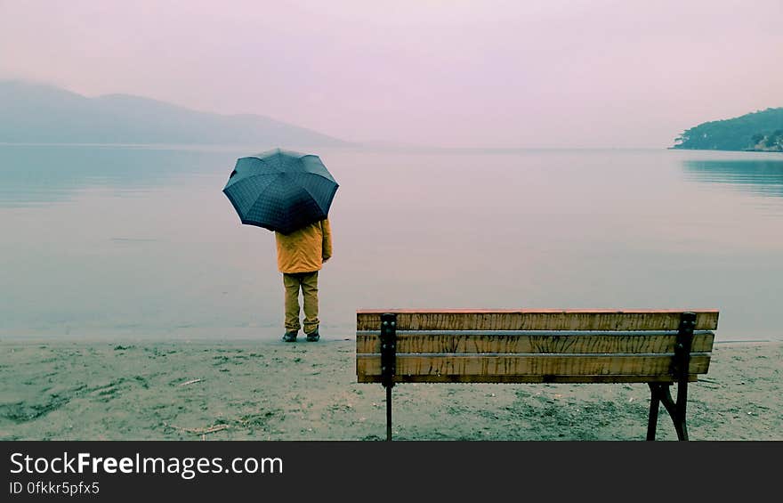 Wet misty day with poor visibility and man beside the sea in yellow jacket holding dark colored umbrella. Wet misty day with poor visibility and man beside the sea in yellow jacket holding dark colored umbrella.