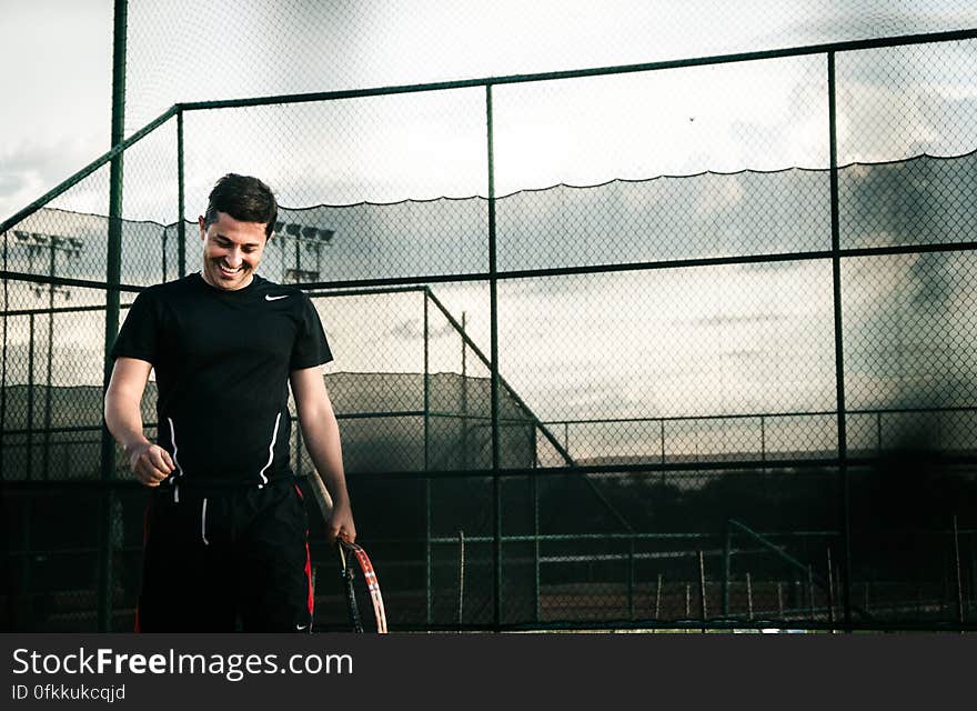 A smiling man out on the tennis court with a tennis racket in hand. A smiling man out on the tennis court with a tennis racket in hand.