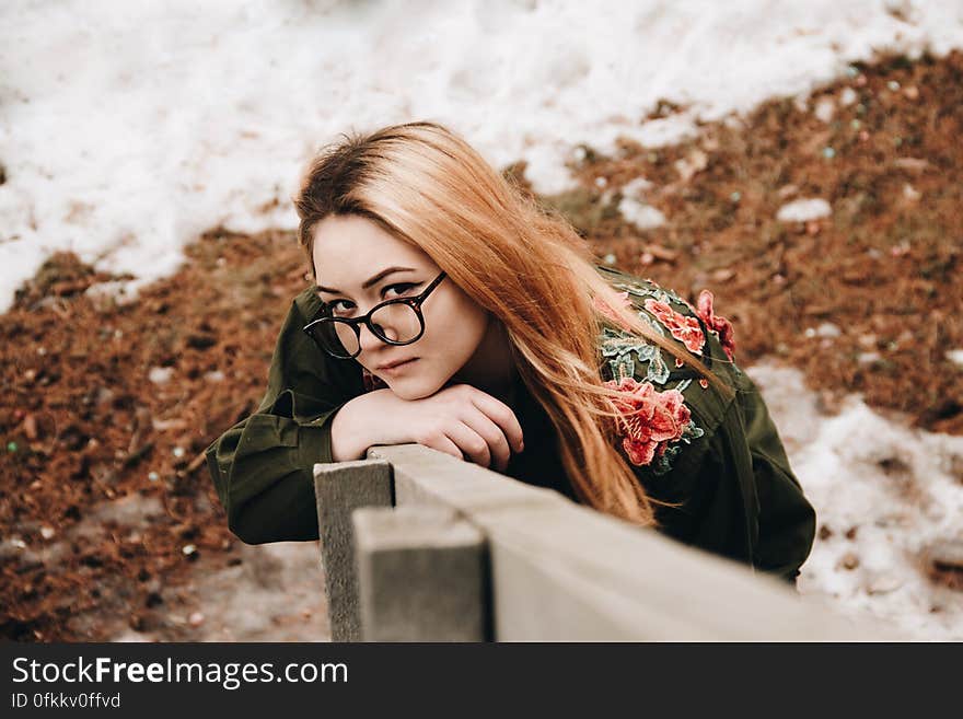 A redhead woman with eyeglasses leaning on a wooden fence. A redhead woman with eyeglasses leaning on a wooden fence.