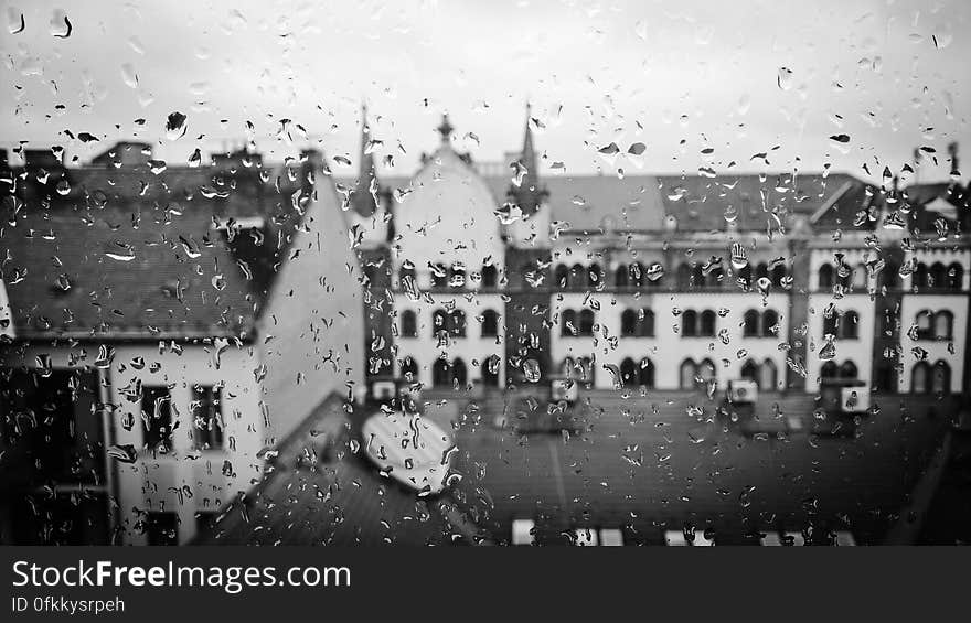 Historic buildings in Hungary seen through a window covered in rain drops, gray sky.