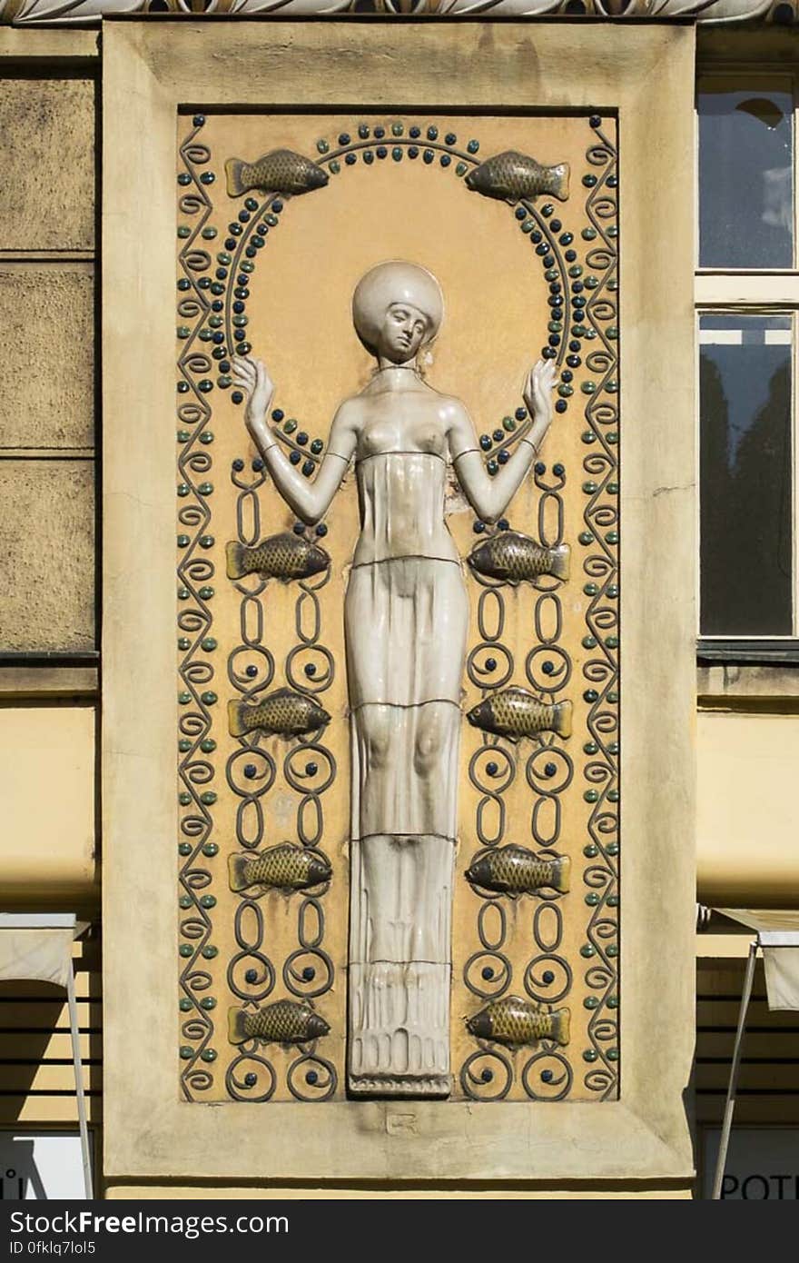 A building decoration in Art Nouveau style, representing a longiline woman figure surrounded by fishes connected by chain links. A building decoration in Art Nouveau style, representing a longiline woman figure surrounded by fishes connected by chain links.