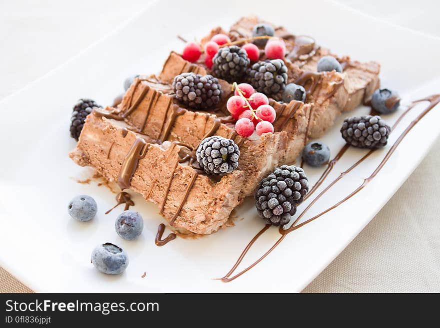 White plate with sliced piece of cake with chocolate drizzle and fresh berries. White plate with sliced piece of cake with chocolate drizzle and fresh berries.