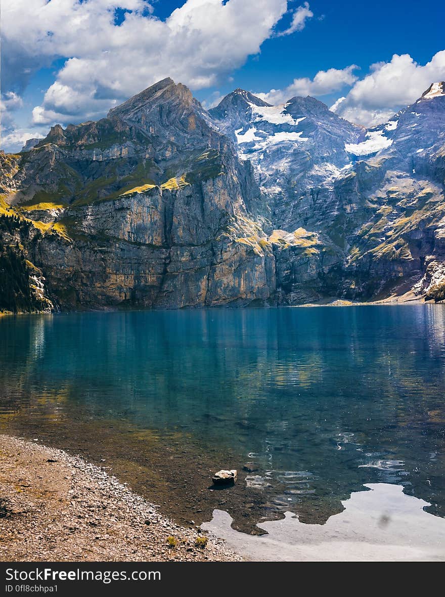 Banks of clear alpine lake surrounded by mountain peaks against blue skies on sunny day. Banks of clear alpine lake surrounded by mountain peaks against blue skies on sunny day.