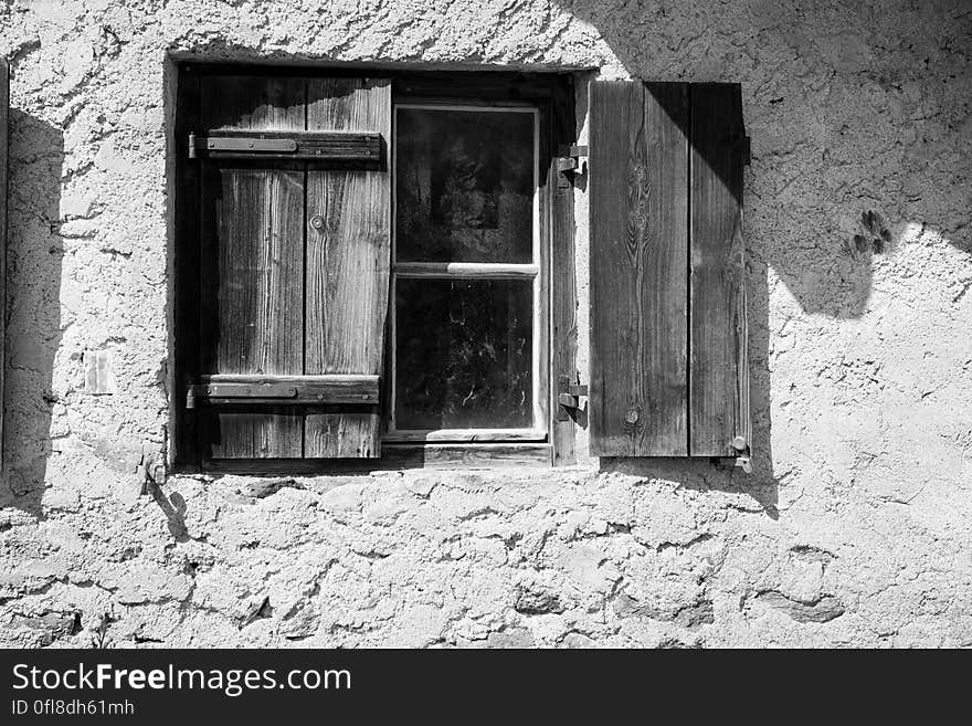 Close up of rustic wooden shutters on window in concrete wall in black and white.