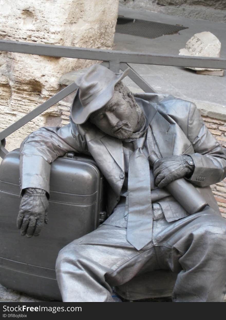 Male street artist covered in silver paint leaning on suitcase with alcohol. Male street artist covered in silver paint leaning on suitcase with alcohol.