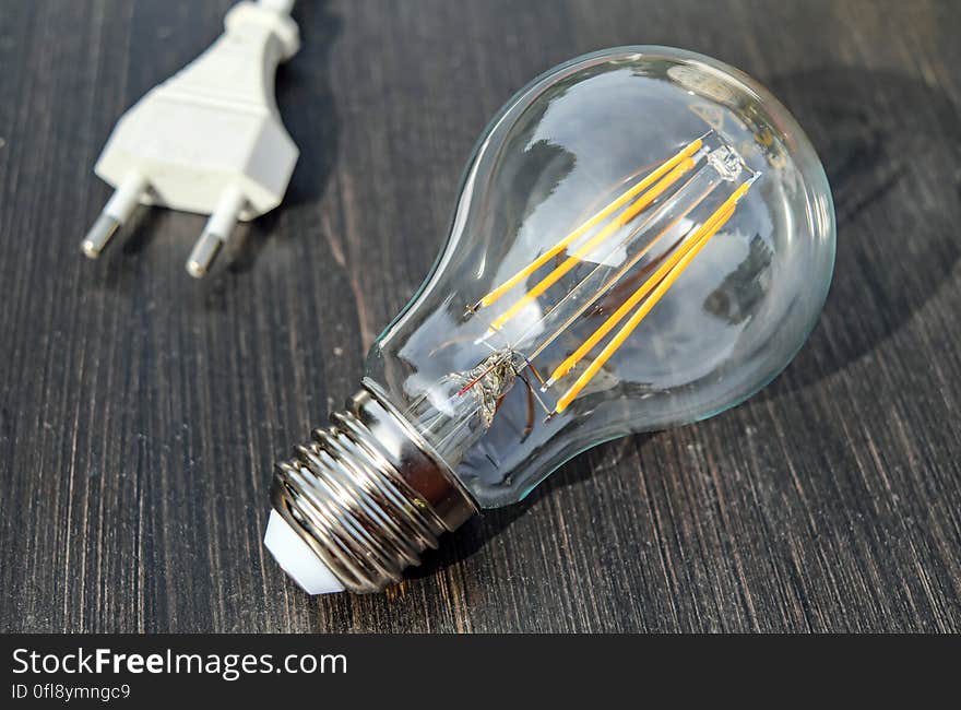 Close up of clear glass filament light bulb on rustic wooden plank with socket plug. Close up of clear glass filament light bulb on rustic wooden plank with socket plug.