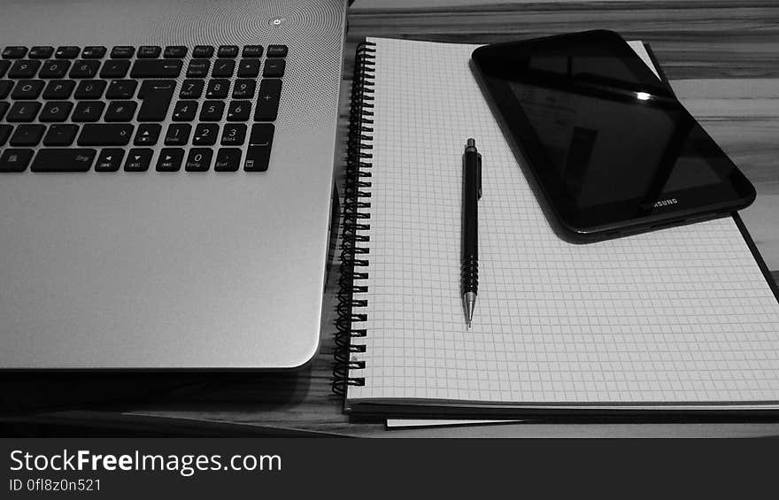 Close up of laptop keyboard with paper spiral notebook and pen on desktop with smartphone. Close up of laptop keyboard with paper spiral notebook and pen on desktop with smartphone.