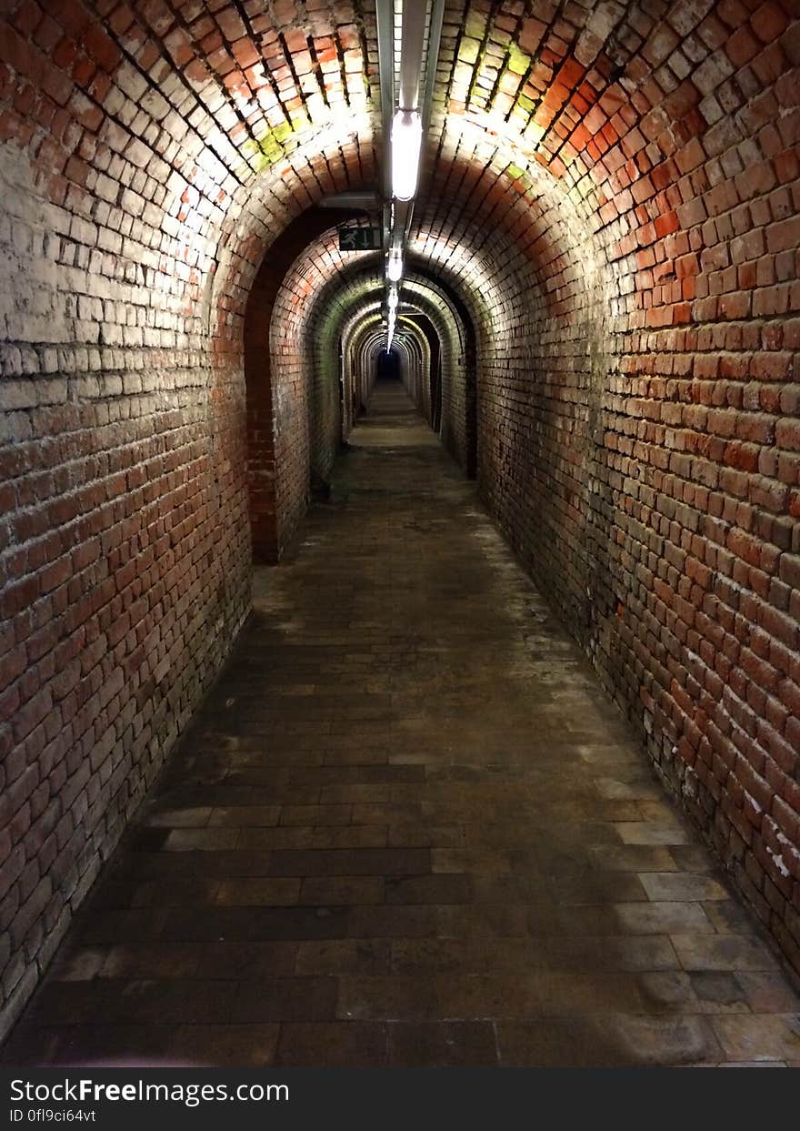 Brick underground passage in old building receding into distance.