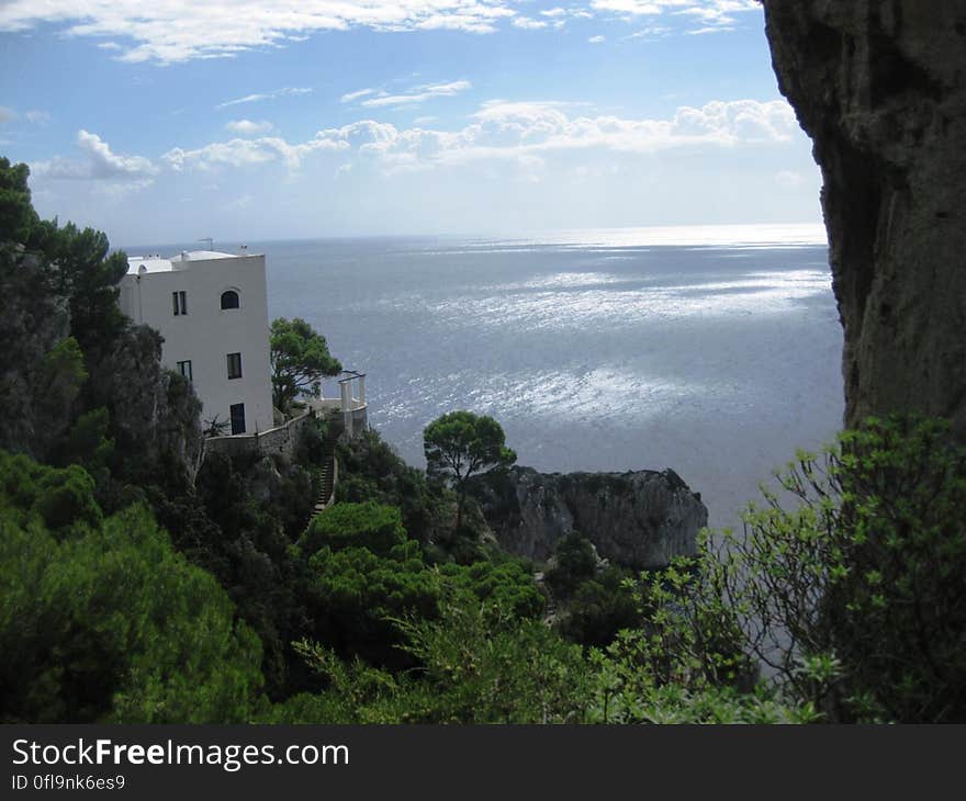 Coastal view from a steep wooded cliff of the tranquil sea with a modern building (apartments) built into the hillside. Coastal view from a steep wooded cliff of the tranquil sea with a modern building (apartments) built into the hillside.