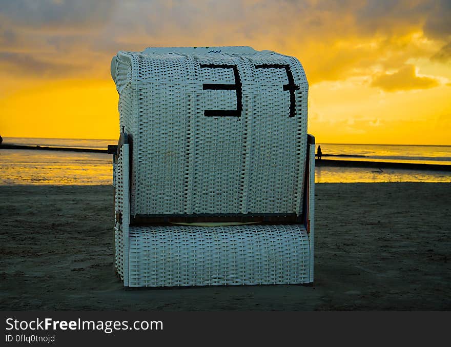 Rear view of large rattan beach chair by ocean with golden sunset background. Rear view of large rattan beach chair by ocean with golden sunset background.