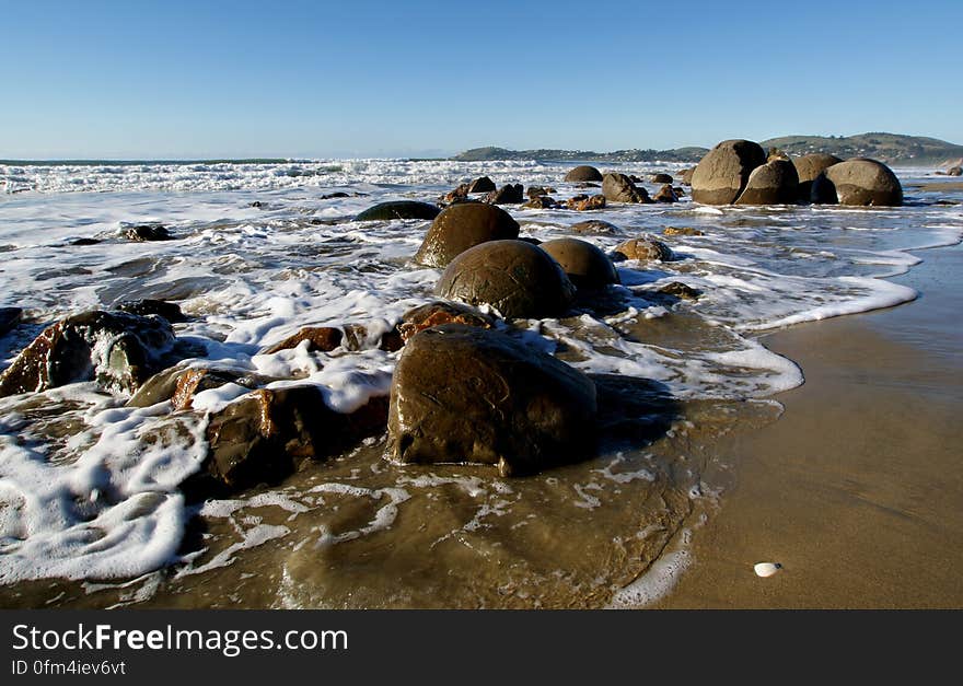 he Moeraki Boulders are unusually large and spherical boulders lying along a stretch of Koekohe Beach on the wave cut Otago coast of New Zealand between Moeraki and Hampden. They occur scattered either as isolated or clusters of boulders within a stretch of beach where they have been protected in a scientific reserve. The erosion by wave action of mudstone, comprising local bedrock and landslides, frequently exposes embedded isolated boulders. These boulders are grey-colored septarian concretions, which have been exhumed from the mudstone enclosing them and concentrated on the beach by coastal erosion. he Moeraki Boulders are unusually large and spherical boulders lying along a stretch of Koekohe Beach on the wave cut Otago coast of New Zealand between Moeraki and Hampden. They occur scattered either as isolated or clusters of boulders within a stretch of beach where they have been protected in a scientific reserve. The erosion by wave action of mudstone, comprising local bedrock and landslides, frequently exposes embedded isolated boulders. These boulders are grey-colored septarian concretions, which have been exhumed from the mudstone enclosing them and concentrated on the beach by coastal erosion