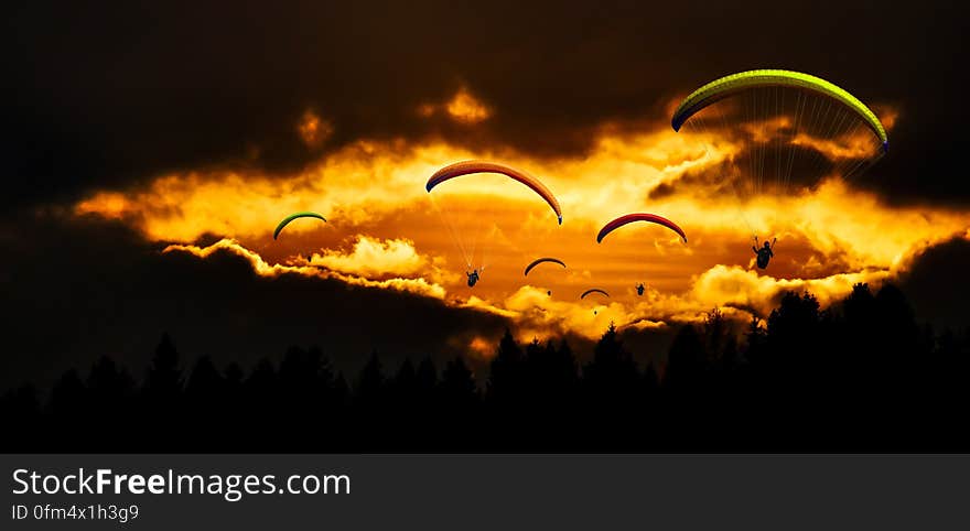 People in Mid Air Using Parachute in Dusk