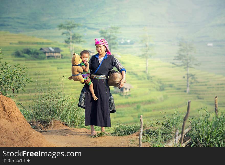 An Asian farmer woman carrying a child near rice terraces. An Asian farmer woman carrying a child near rice terraces.