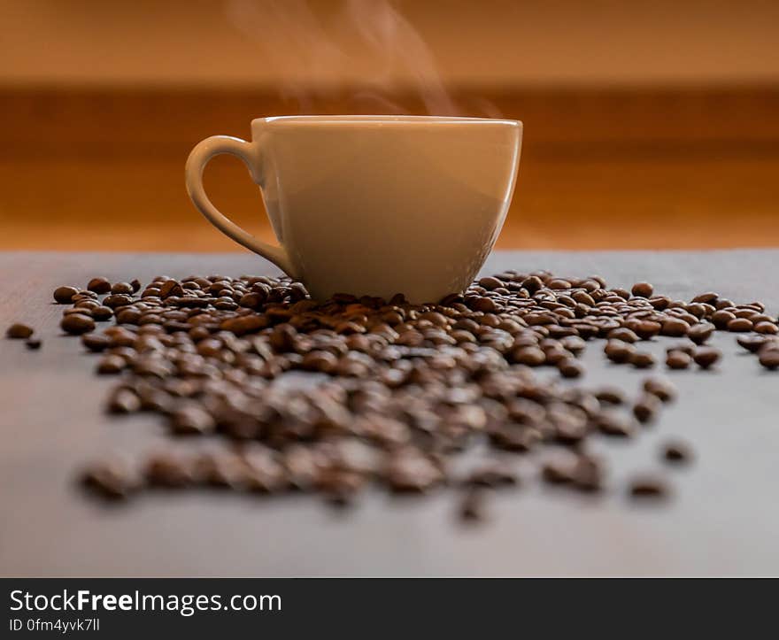 Scattered coffee beans on table with steaming hot cup in background. Scattered coffee beans on table with steaming hot cup in background.