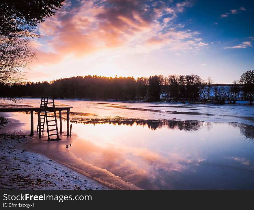 Wooden dock on river waterfront at dusk in countryside.