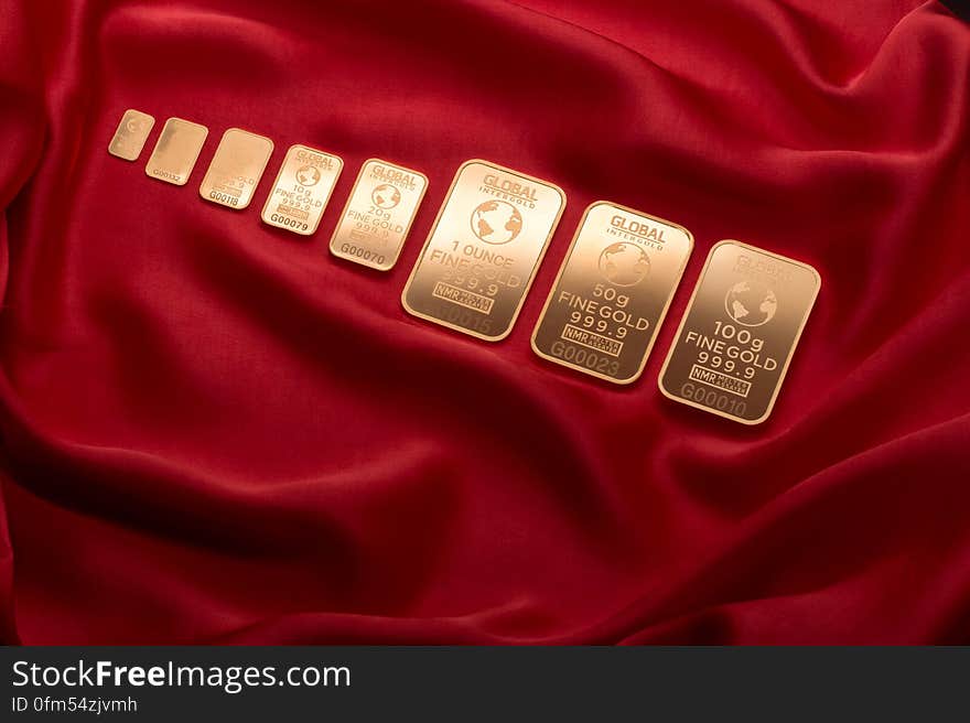 Row of golden bars with globe symbol on crumpled red velvet background. Row of golden bars with globe symbol on crumpled red velvet background.