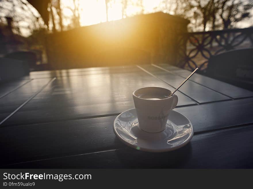 Coffee cup and saucer with spoon on tabletop outside at sunrise. Coffee cup and saucer with spoon on tabletop outside at sunrise.