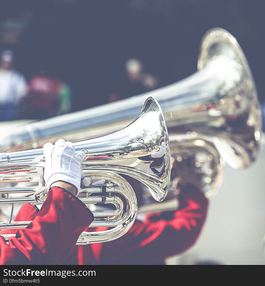 Close up of trumpet horns in marching band held by uniformed musicians wearing white gloves.