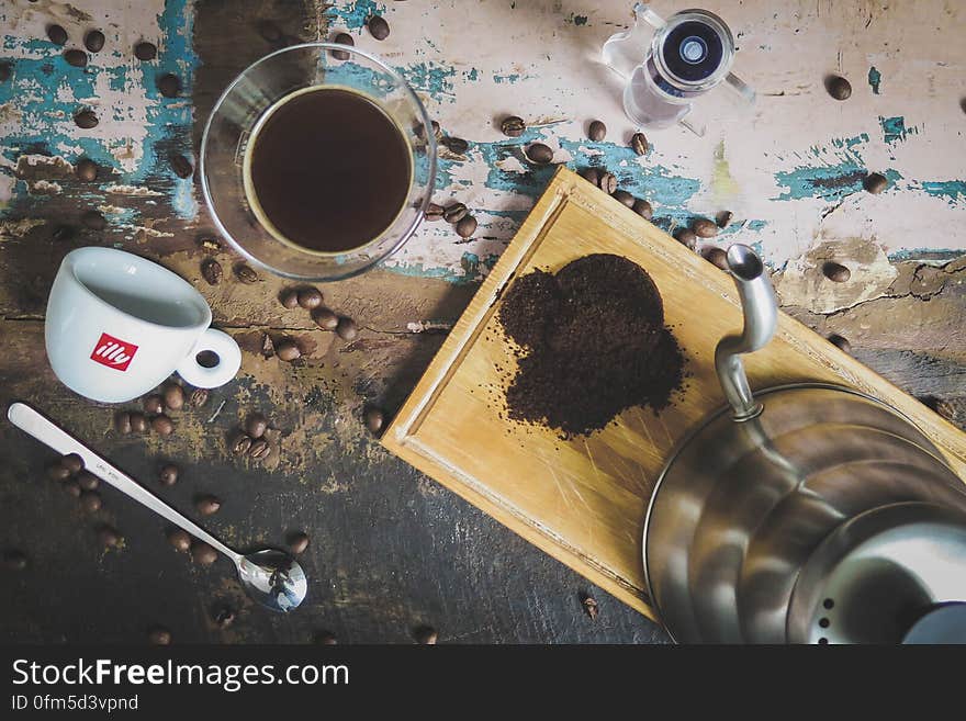 Coffee grinder, glass, grinded coffee, cup, teaspoon and coffee beans on a table. Coffee grinder, glass, grinded coffee, cup, teaspoon and coffee beans on a table.