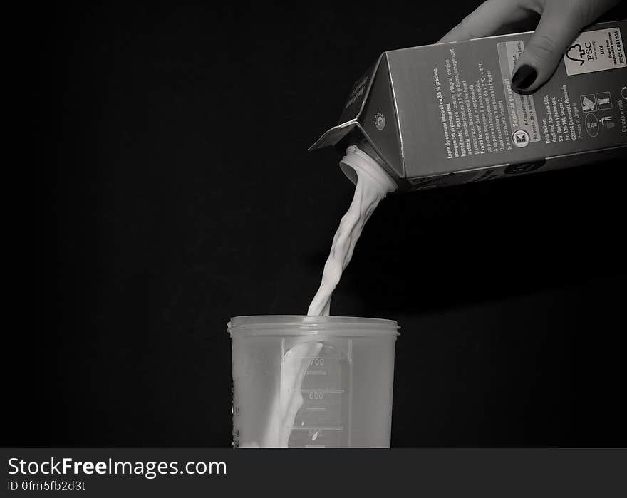 A black and white close up of a woman`s hand pouring milk into a plastic cup. A black and white close up of a woman`s hand pouring milk into a plastic cup.