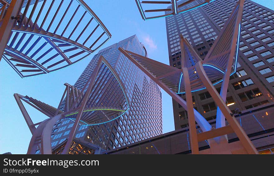 Metal art outside modern skyscrapers against blue skies on sunny day.