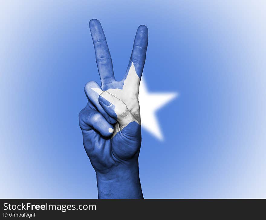 A hand doing the V sign in front of a flag with white star. A hand doing the V sign in front of a flag with white star.