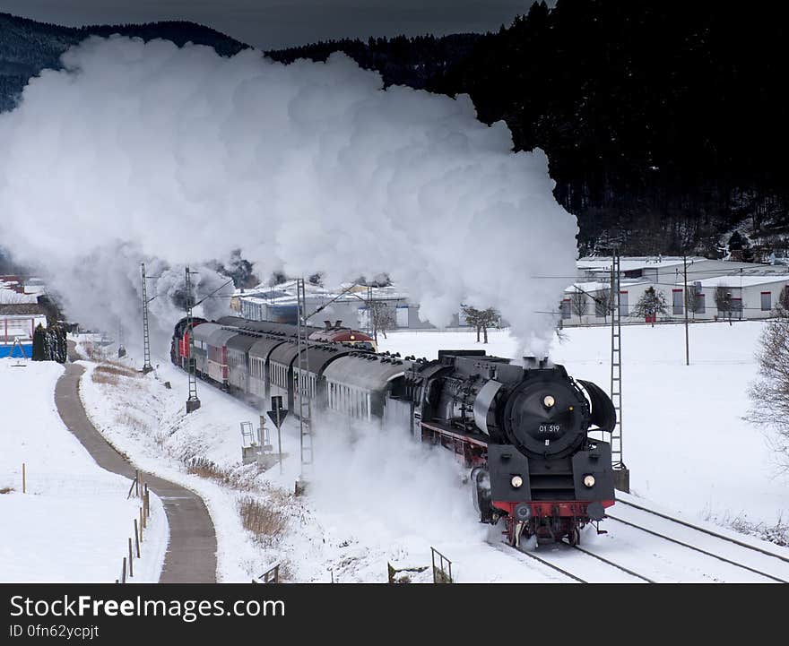 Steam engine pulling train cars on tracks through snow in countryside. Steam engine pulling train cars on tracks through snow in countryside.