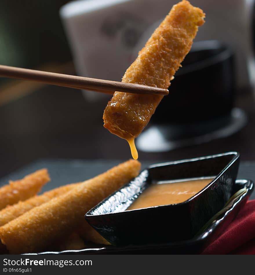 Close up of chopsticks holding piece of fried pork over dish of dipping sauce. Close up of chopsticks holding piece of fried pork over dish of dipping sauce.