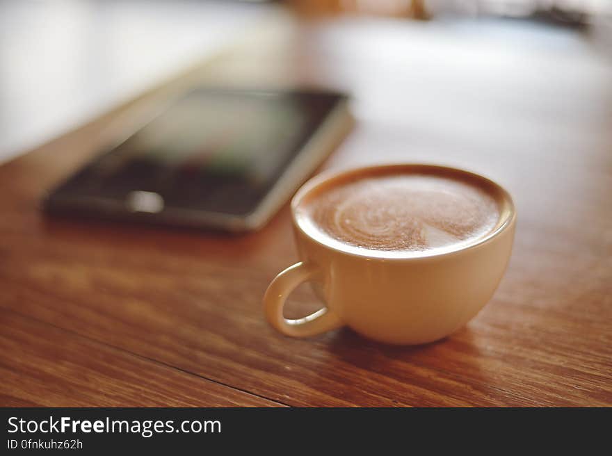 A cup of coffee on a table next to a mobile phone.