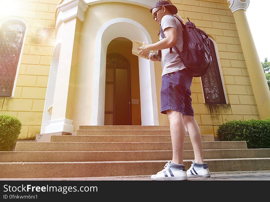 low angle view of young male backpacker stood outside building entrance with guidebook, sunlight effect. low angle view of young male backpacker stood outside building entrance with guidebook, sunlight effect.