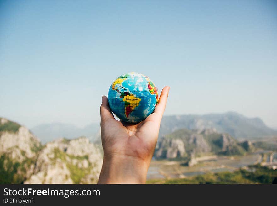 Close up of hand holding globe in scenic landscape.